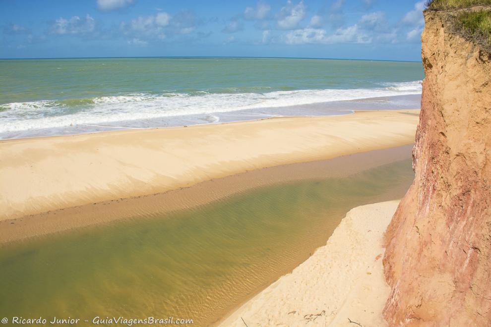 Imagem do mar, uma pequena faixa de areia e piscina natural em Cumuruxatiba.